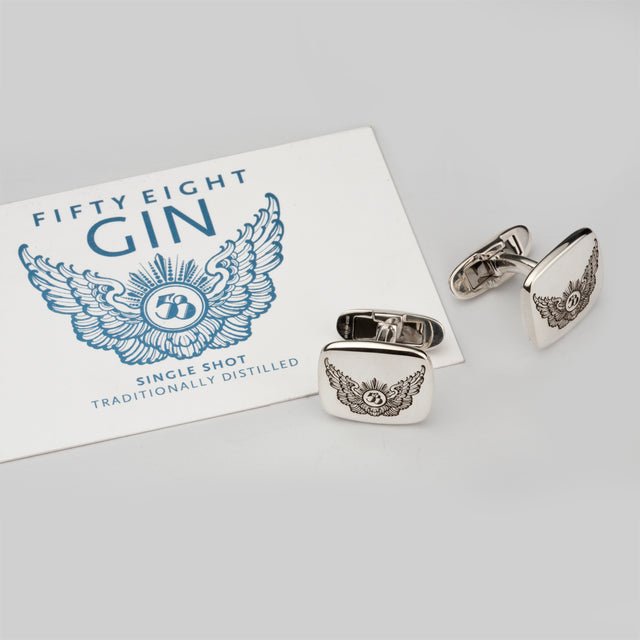 A silver pair of cufflinks with a wing engraving logo on them next to a business card of Fifty Eight Gin with the same logo.